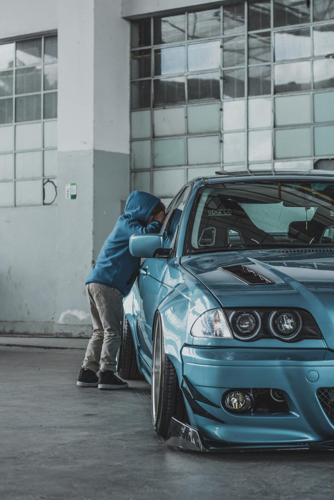 Young child in blue jacket peers into a sleek modern car indoors.